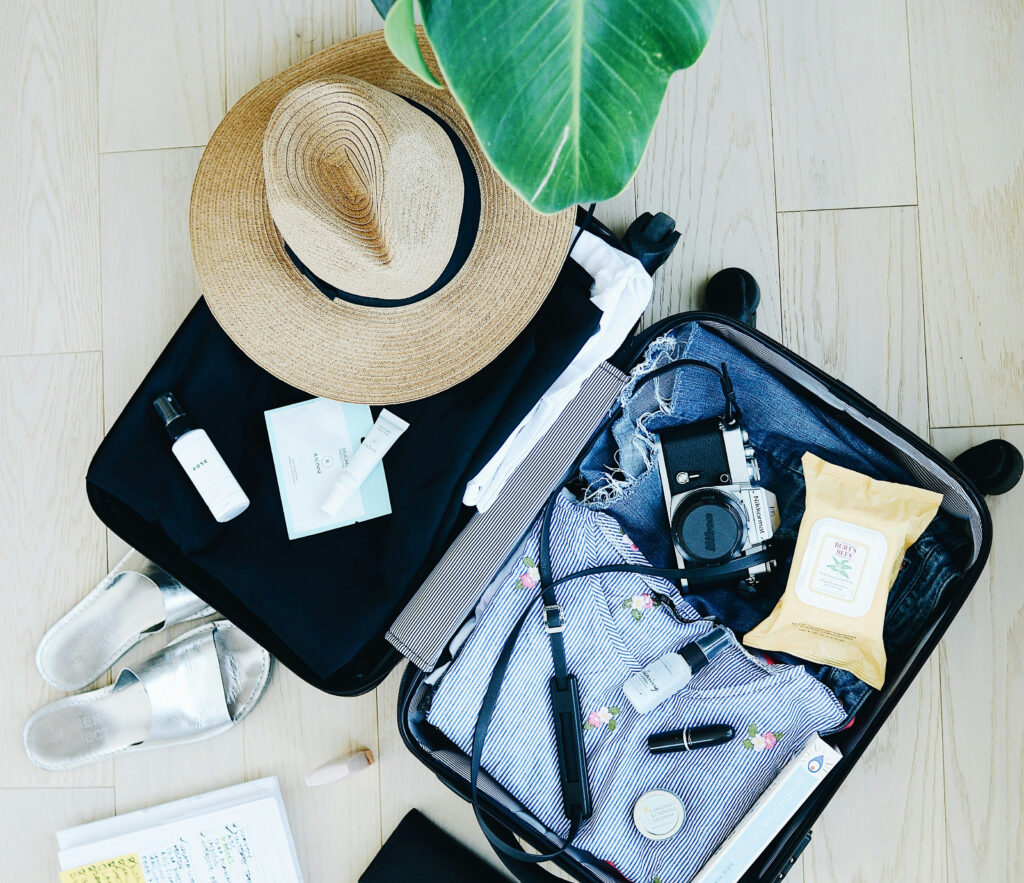 Photo of an open suitcase with clothes, a camera, and a hat.